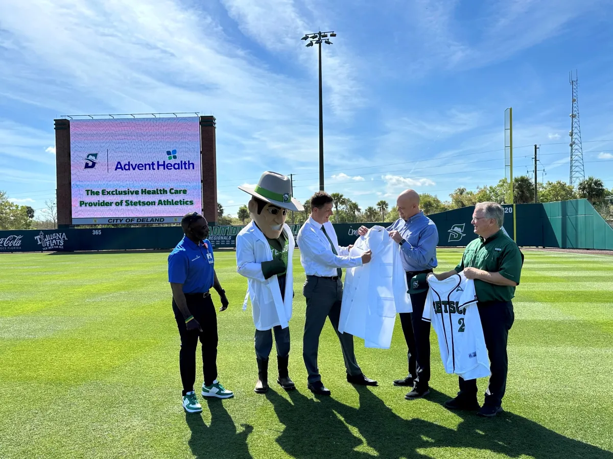 Eric Lunde, president and CEO of AdventHealth DeLand presents lab coat to Stetson University President, President, Chrisopher F. Roellke, PhD.